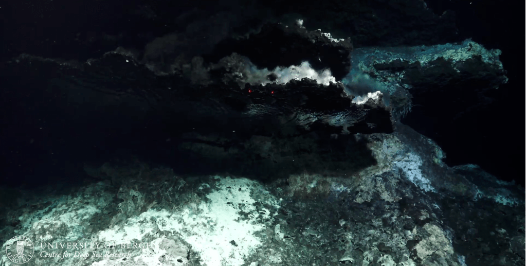 A hydrothermal vent chimney with shimmering fluids and white bacterial mats.